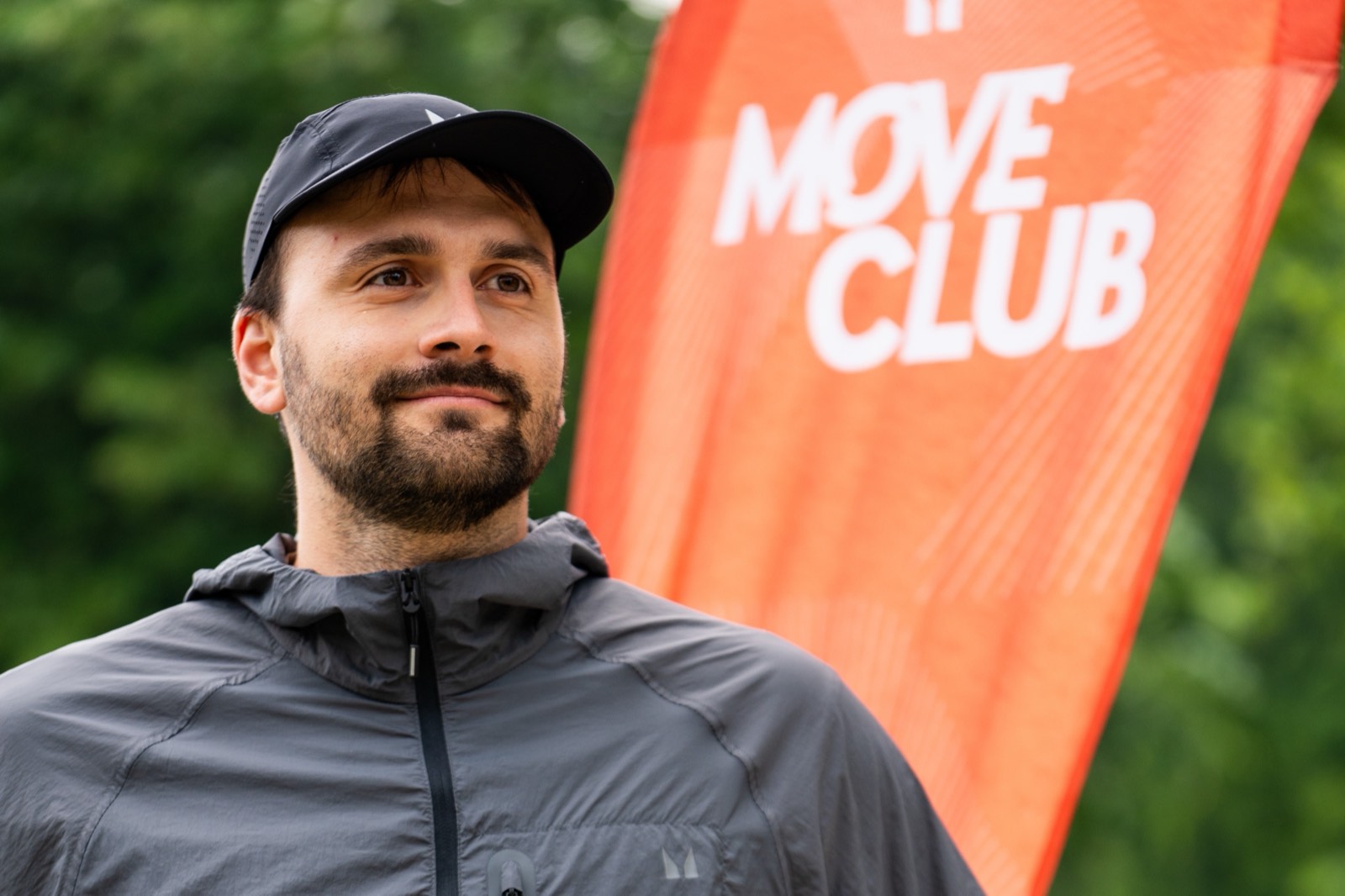 Rácz Gergő futóedző egy Move Club futóesemény zászlaja előtt áll a parkban.